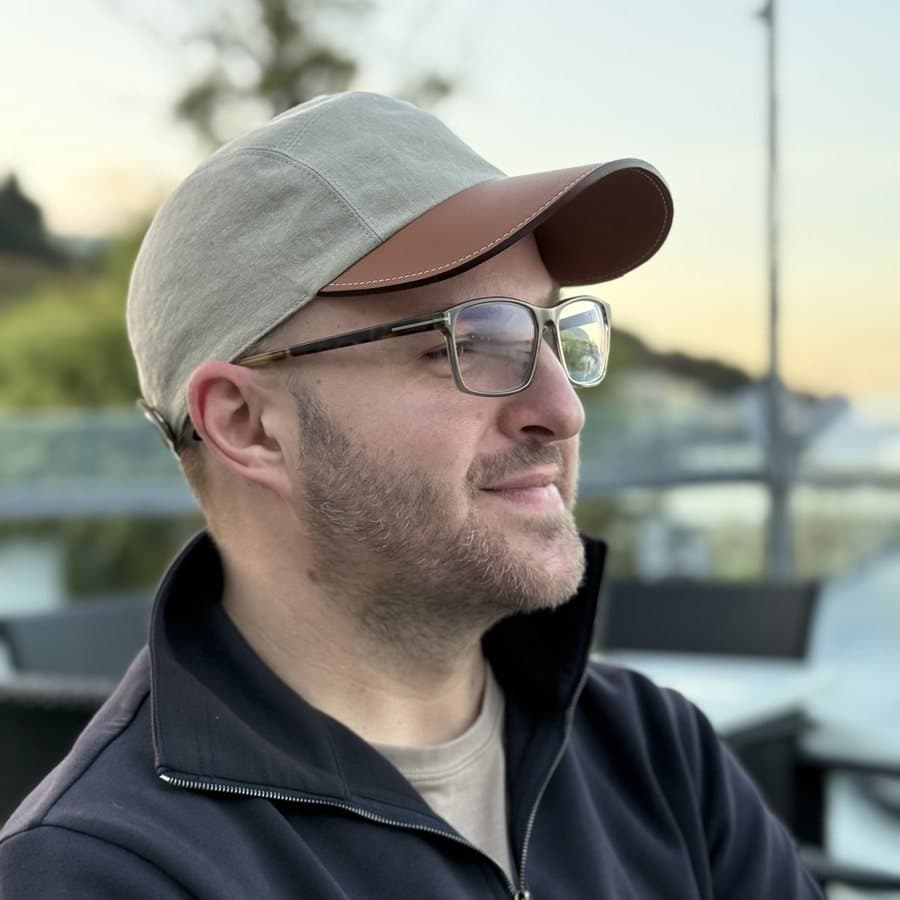 Curtis Crimmins in a cap and glasses, arms folded, looking off to the side at dusk.